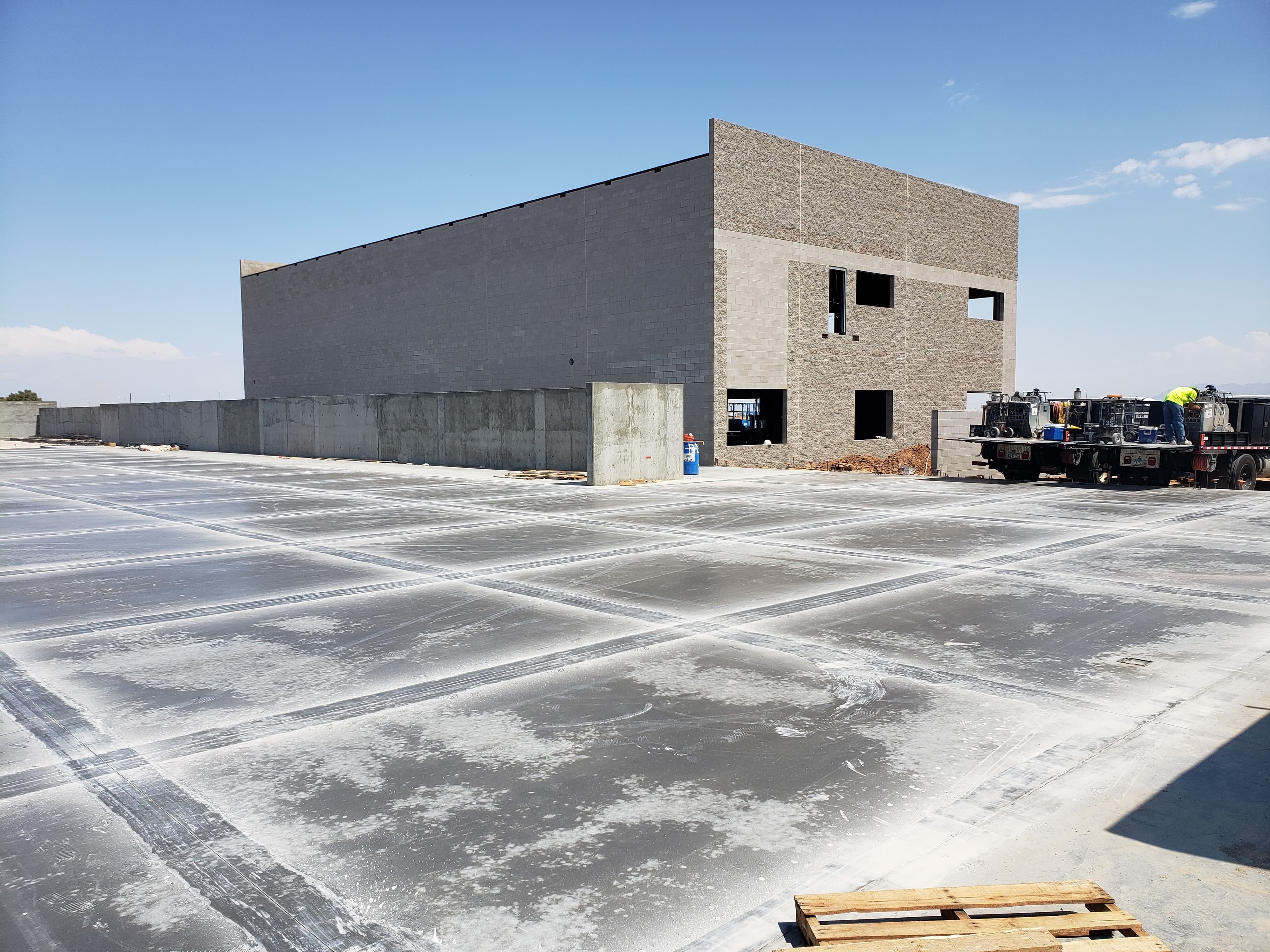 Large concrete slab with grid markings before an unfinished grey block building under blue sky.