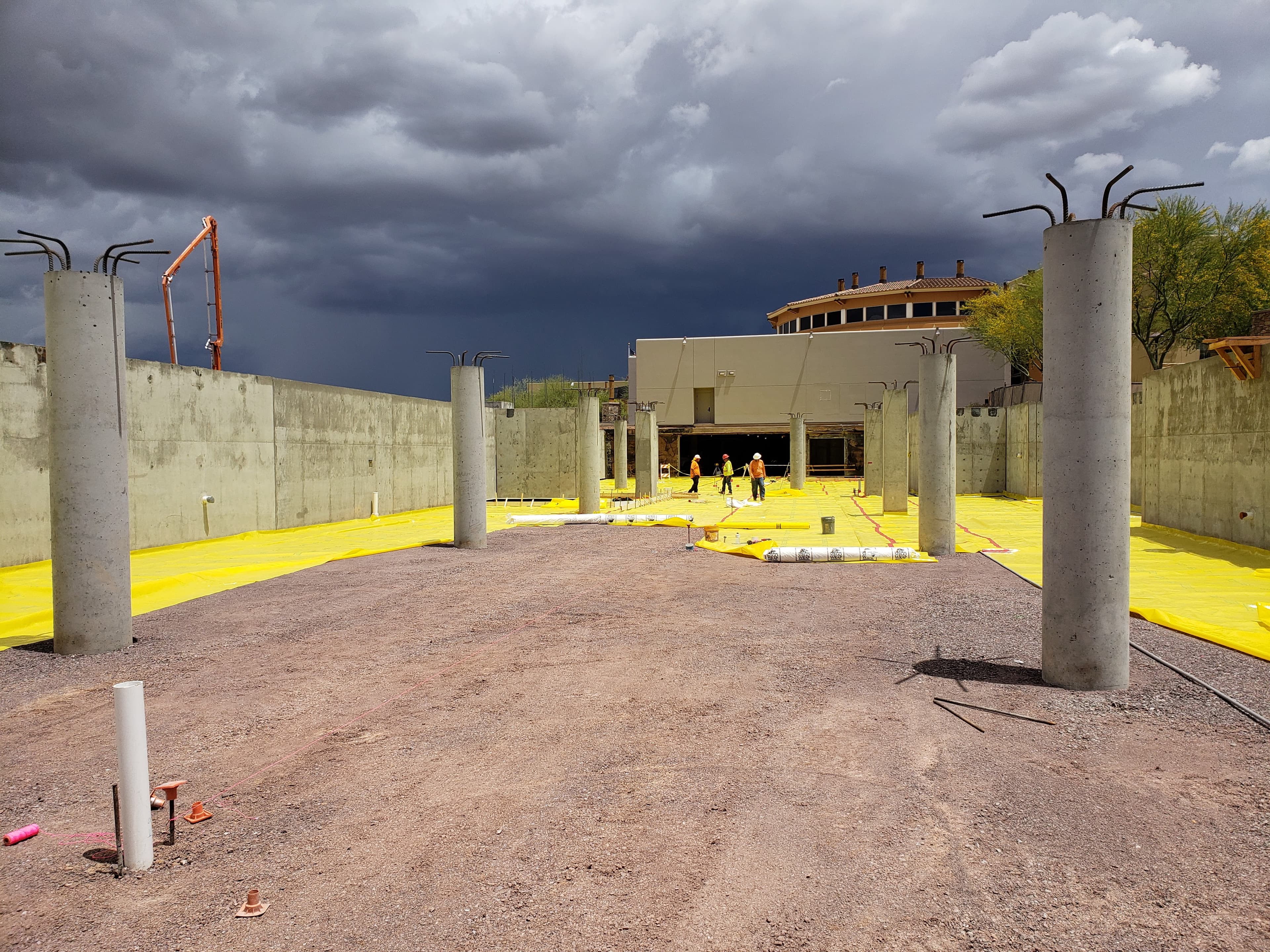 Concrete pillars and yellow vapor barrier at a construction site under dark, stormy clouds.