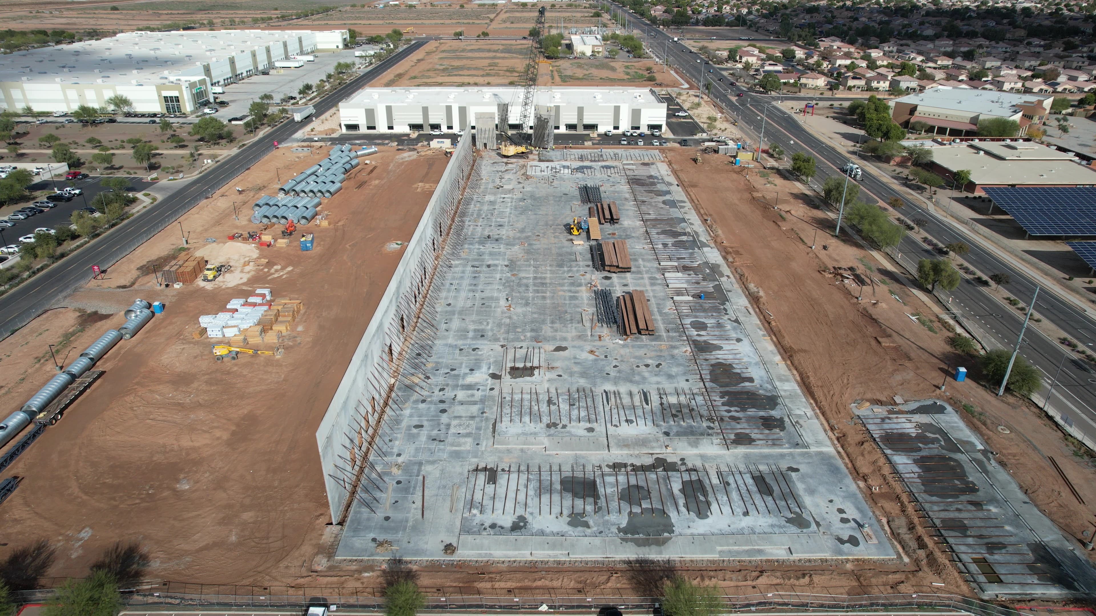 Aerial view of a large construction site featuring a concrete foundation and a rising wall.