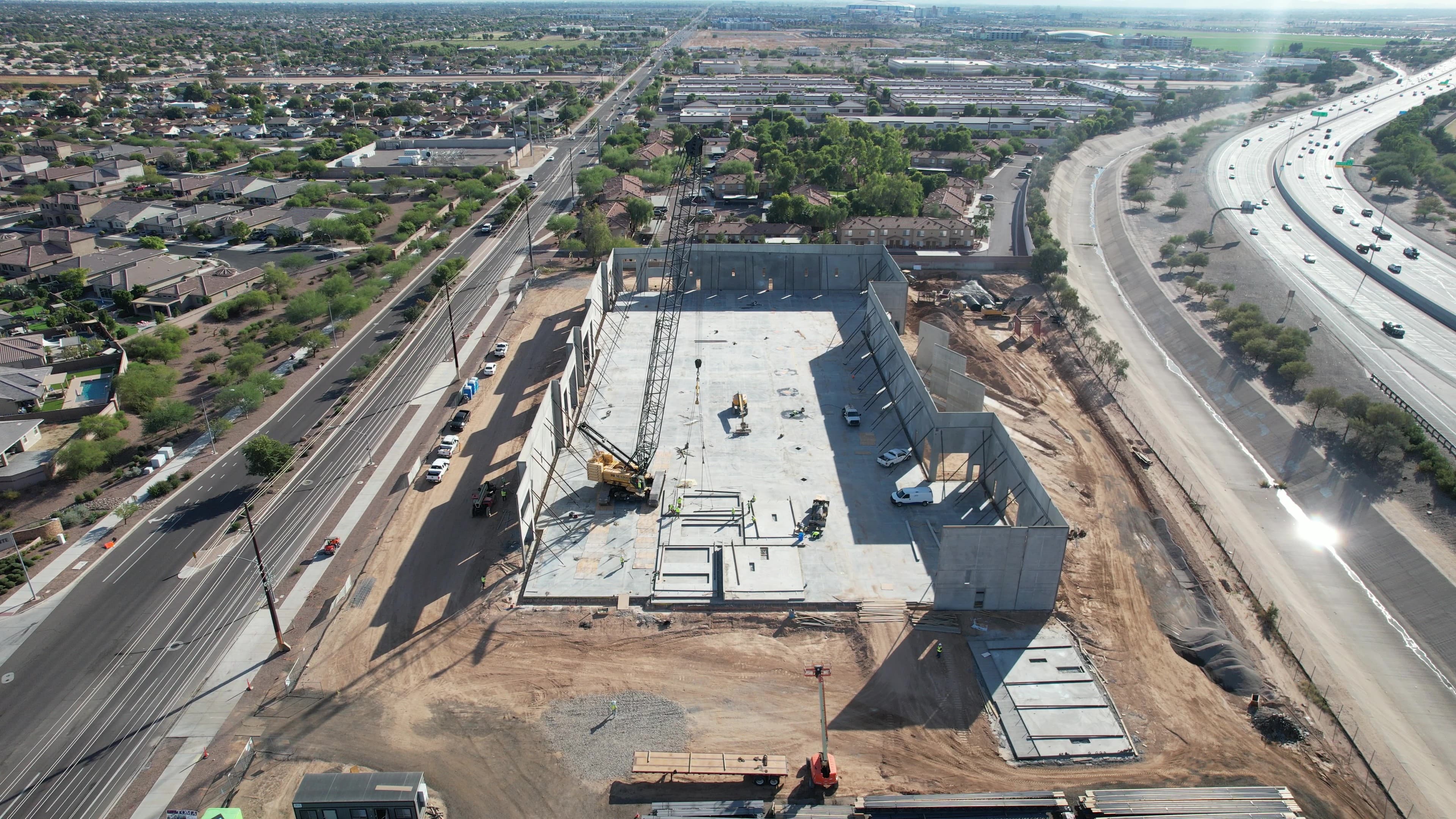 Aerial view of a large concrete building under construction with a crane near a highway.